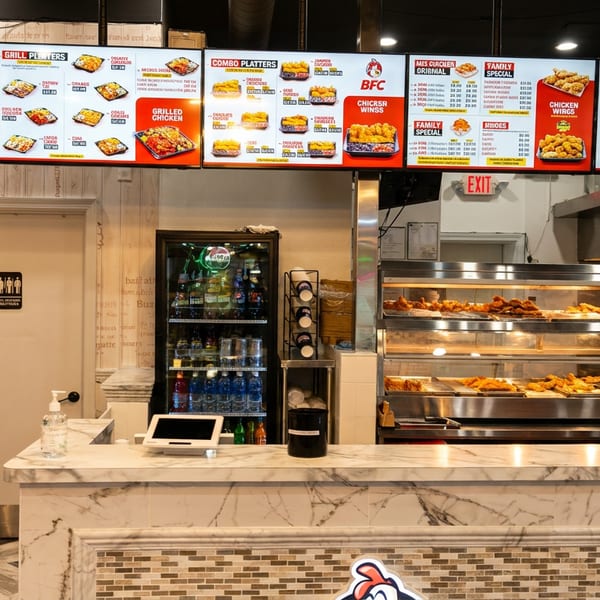 Interior of BFC restaurant with menu boards, a marble counter, and food warmers filled with fried chicken.