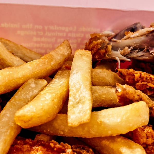 Close-up of golden french fries and crispy fried chicken pieces in a pink box.