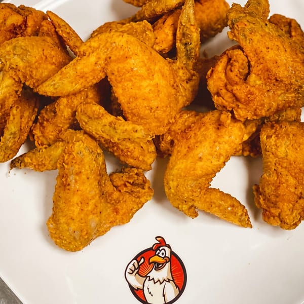 A white rectangular plate filled with golden-brown fried chicken wings, with a chicken logo at the bottom.